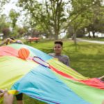 Kids enjoying a fun outdoor game with a colorful parachute and ball in a park setting.