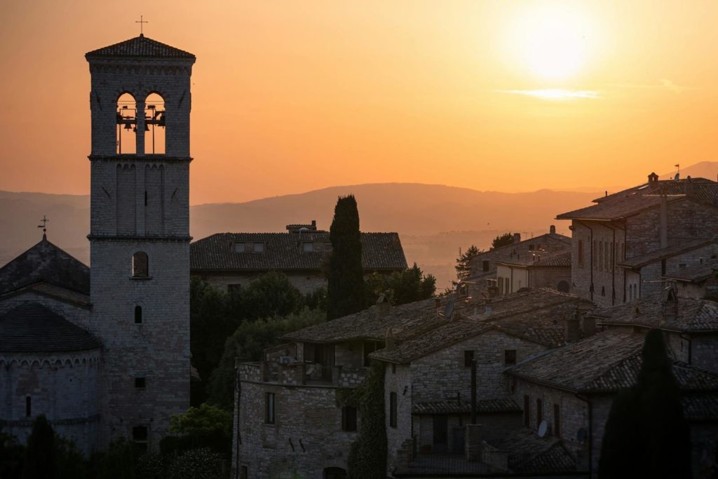 Stunning sunset over the historic stone buildings of Assisi, Italy with a bell tower in view.